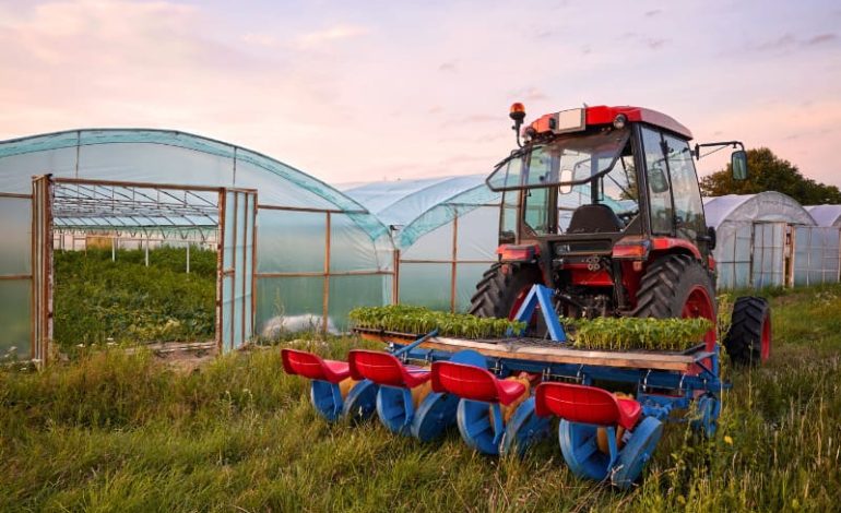 Trator na cor vermelha ao lado de estufas agrícolas